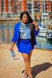 Woman in a blue outfit standing by a waterfront with buildings in the background