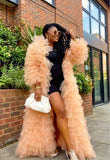 Woman in a peach ruffled coat and black outfit standing outdoors near a building.