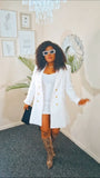 Woman in a white coat and knee-high boots standing in a room with decor elements.