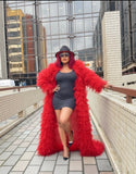 Woman wearing a red fur coat and black dress on a rooftop with cityscape background