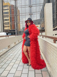 Person wearing a long red fur coat and black hat on a rooftop with cityscape background