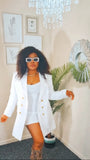 Woman in a white outfit with gold buttons standing in a room with a chandelier and framed pictures.