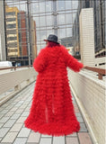 Person wearing a long red luxury tulle coat walking on a rooftop with cityscape background