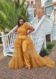 Woman in a yellow ruffled luxury red carpet outfit on a brick patio with a white staircase and greenery in the background.