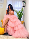 A woman wearing a voluminous light pink tulle ball gown. The dress features a sweetheart neckline and a tiered, ruffled tulle skirt.
