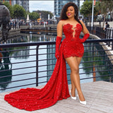 A woman stands on a waterfront promenade wearing a bright red embellished evening gown with long matching gloves and white pointed heels. The dress has a plunging neckline, fitted bodice, and a long train with a sparkly sequin finish.